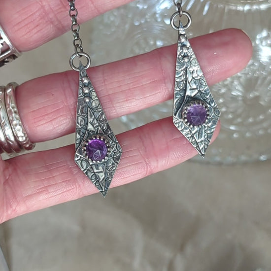 Close-up video of the Maiden Earrings resting in a jeweller's hand, with the recycled silver catching the light and shining beautifully. In the background, a crystal teacup adds an elegant touch, enhancing the delicate craftsmanship of the earrings.

