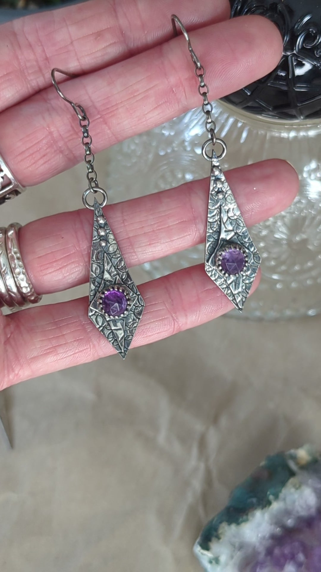 Close-up video of the Maiden Earrings resting in a jeweller's hand, with the recycled silver catching the light and shining beautifully. In the background, a crystal teacup adds an elegant touch, enhancing the delicate craftsmanship of the earrings.

