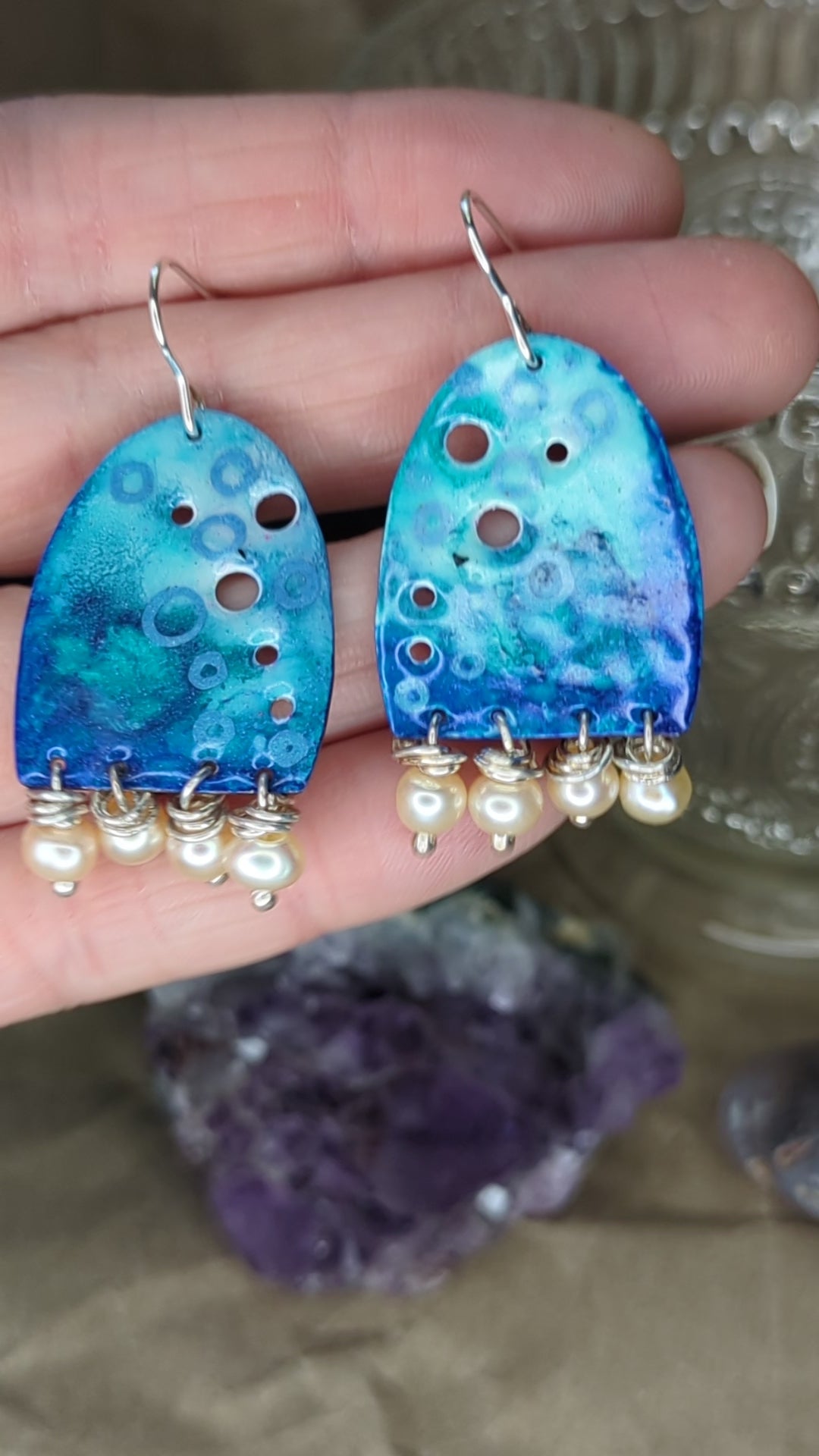 Video of blue enamel earring adorned with apricot freshwater pearls, placed on a hand, the earrings are moving to show all the blue colours 