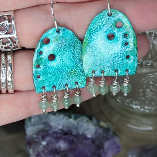 Video of turquoise enamel earrings adorned with green adventurine beads, placed on a hand, the earrings are moving to show all the turquoise colours 
