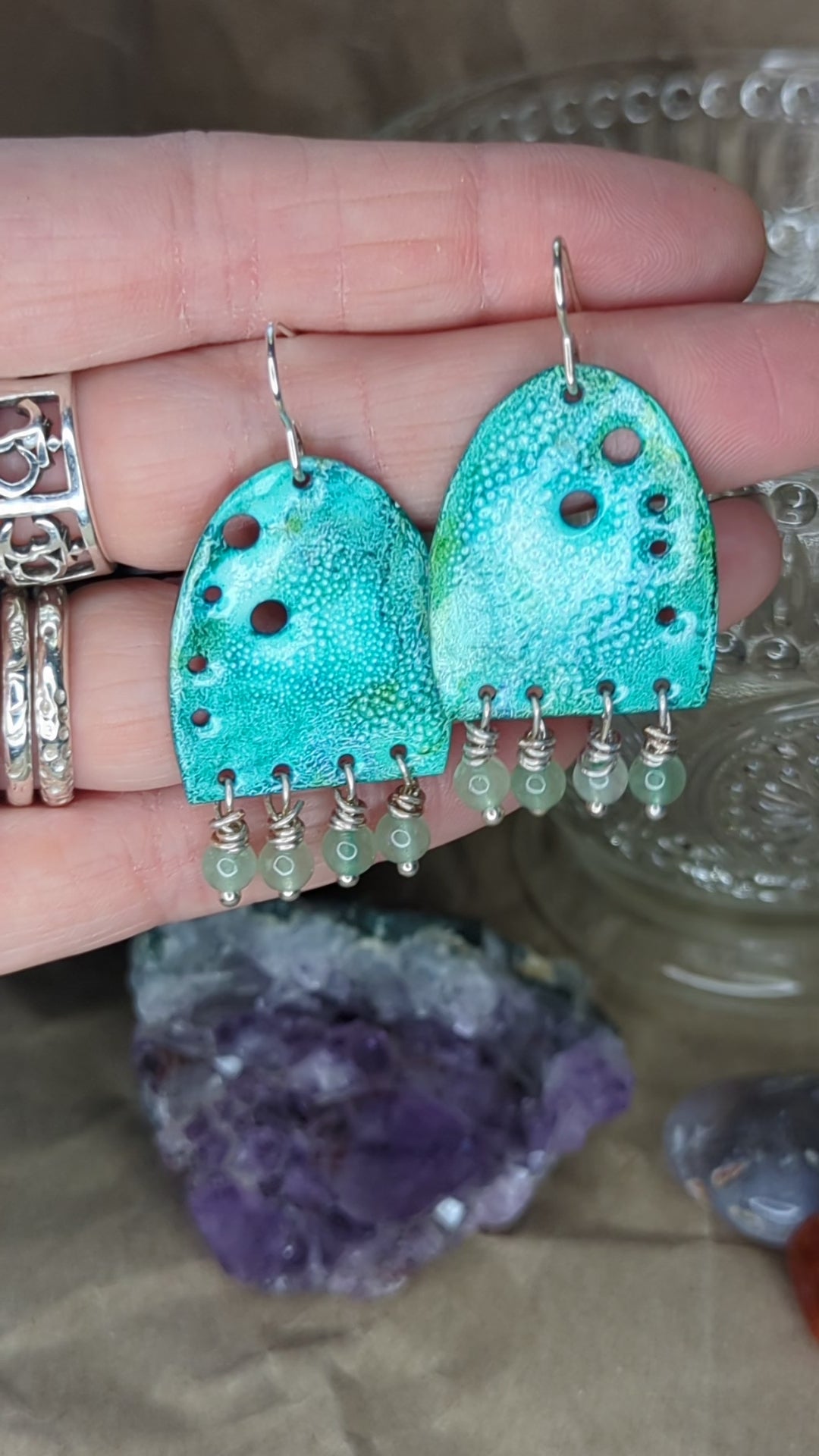 Video of turquoise enamel earrings adorned with green adventurine beads, placed on a hand, the earrings are moving to show all the turquoise colours 