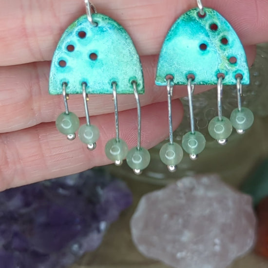 Video of turquoise enamel earrings adorned with green adventurine beads, placed on a hand, the earrings are moving to show all the turquoise colours 