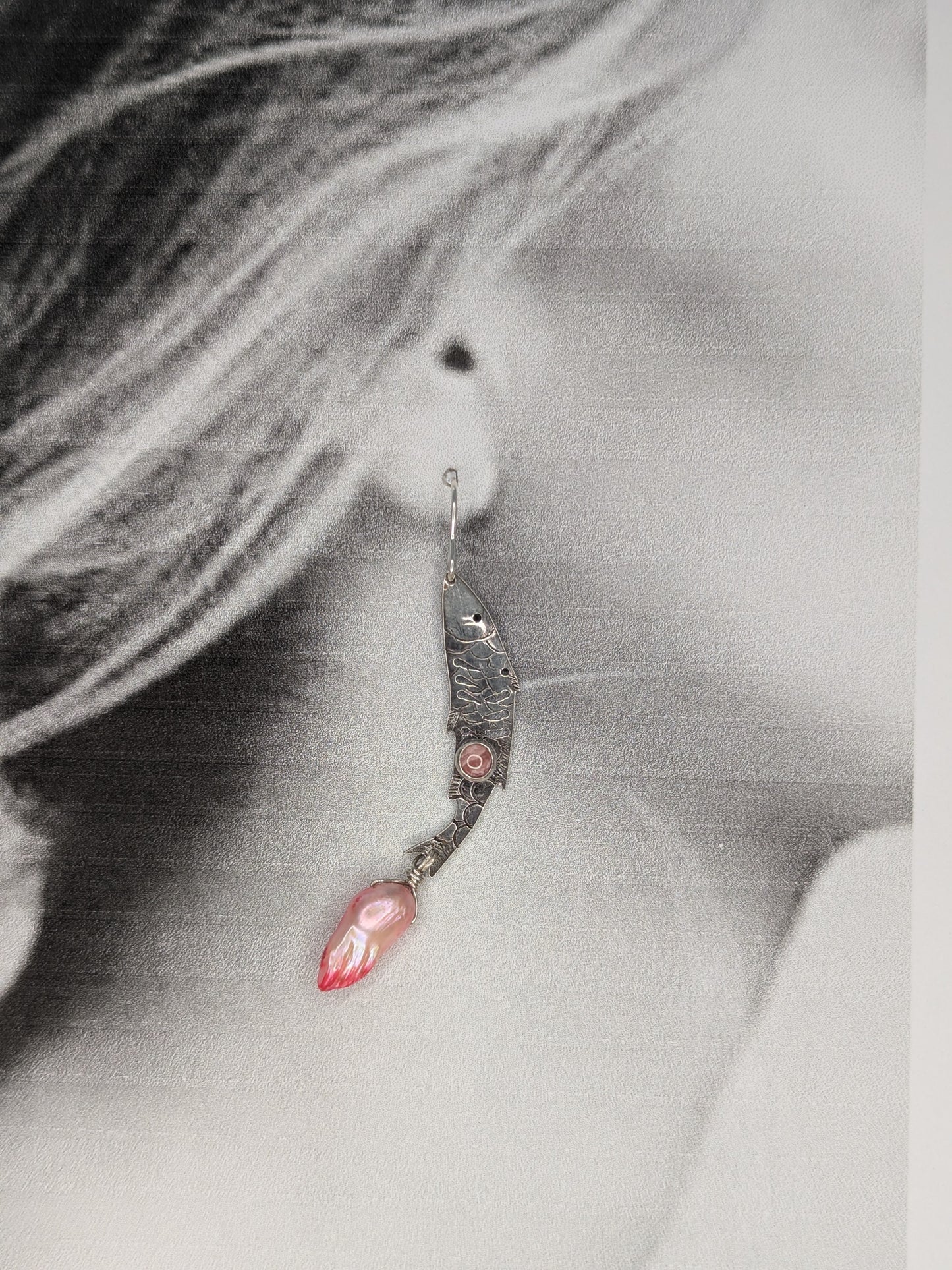 Sterling silver fish earrings, with fish details engraved on the silver, adorned with pink Rhodochrosite Cabochons and Pink keshi Freshwater Pearls. The earrings are placed on a black and white image of a model to show the earrings in the ear lobe. 