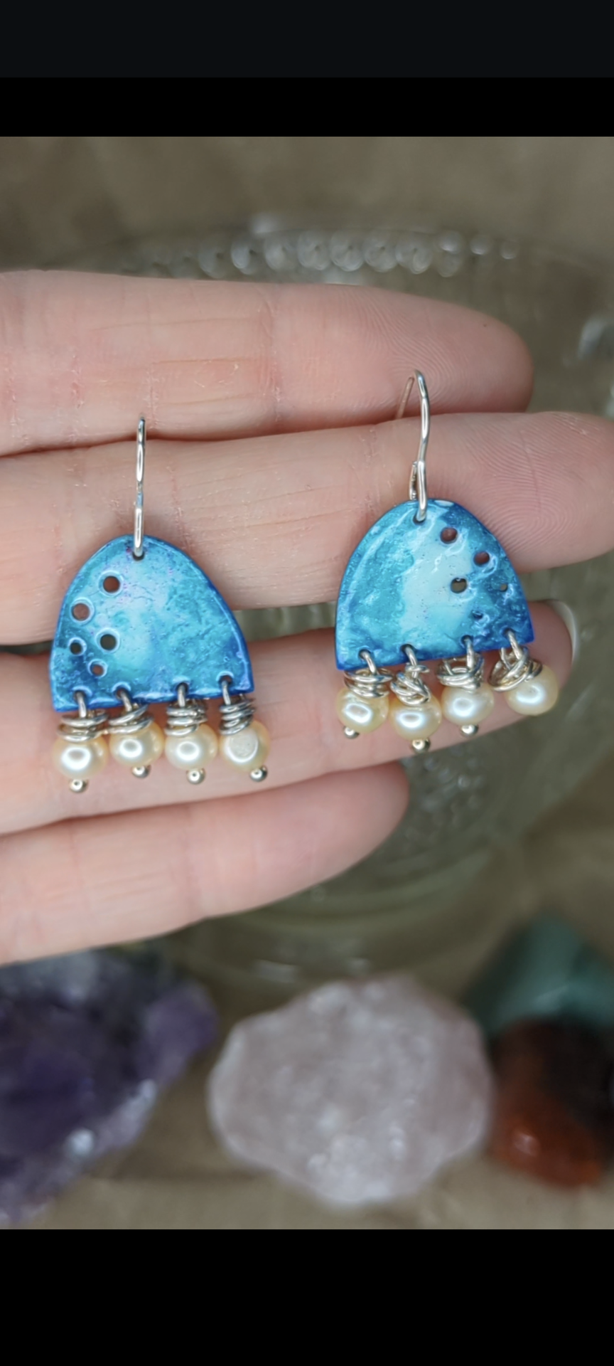Blue enamel earrings with colours of blue with apricot freshwater pearls, Earrings are placed on hands to show the contrast with the earrings against skin.