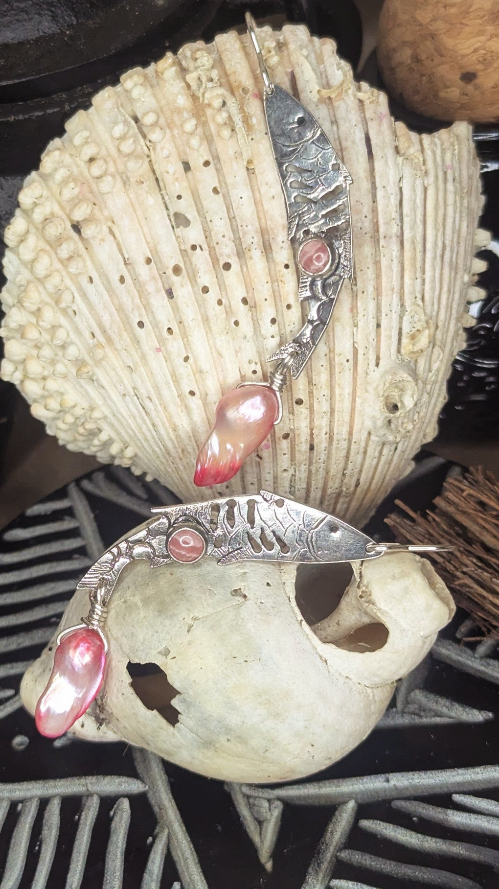 Sterling silver fish earrings, with fish details engraved on the silver, adorned with pink Rhodochrosite Cabochons and Pink keshi Freshwater Pearls. Each earring is placed on a large sea shell. 
