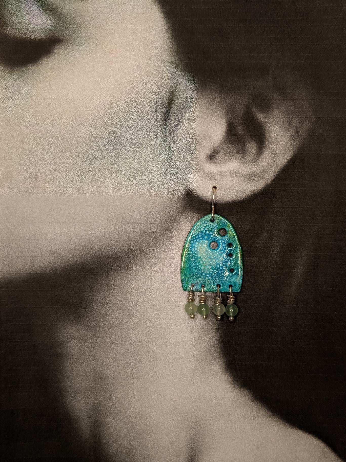 Black and white image of a model wearing turquoise earrings with green aventurine beads. 