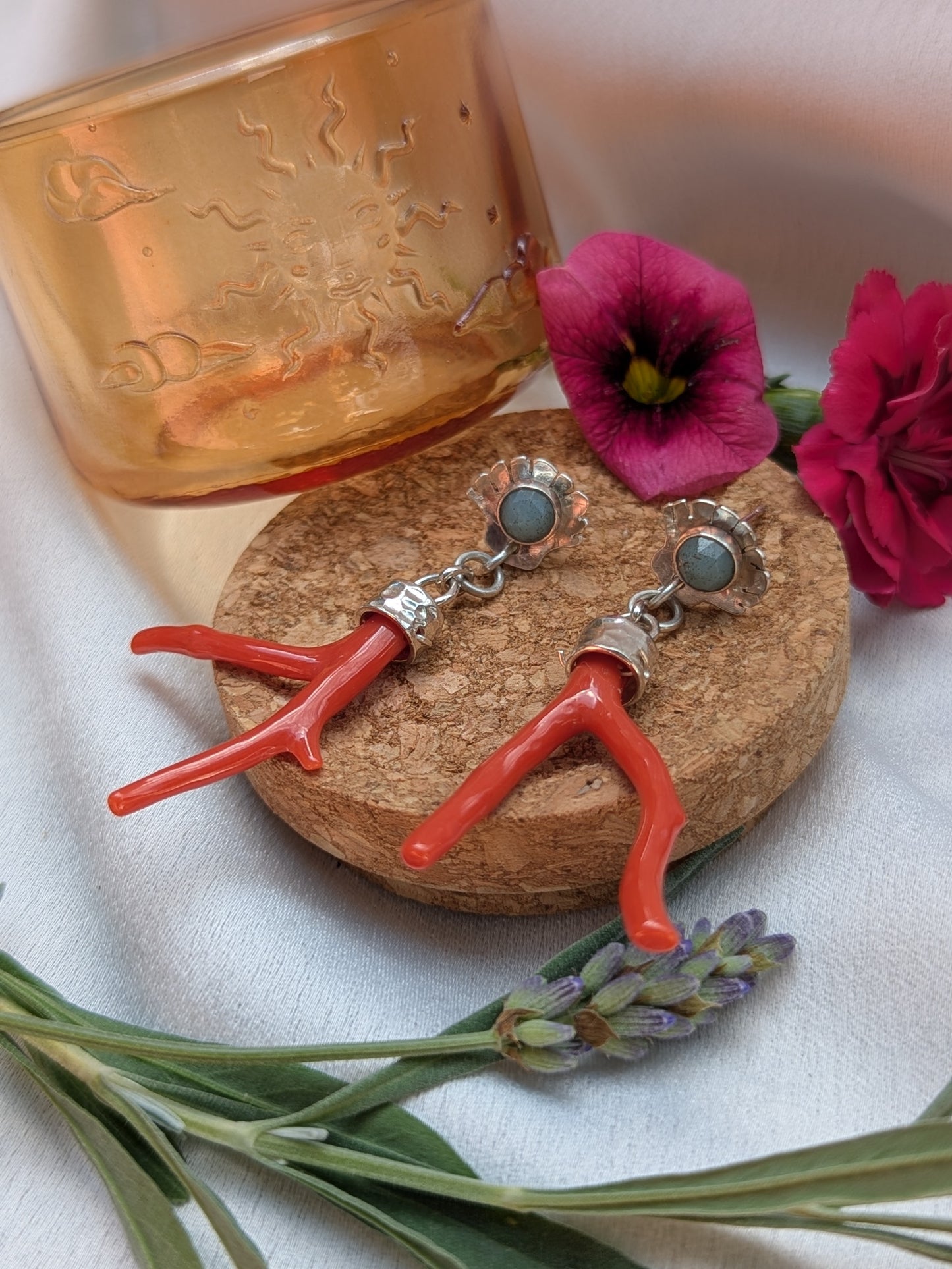 Sterling silver stud earrings styled on an cork plinth, featuring a rose-cut turquoise stone set in scallop shell studs, with red coral branch drops hanging below. Surrounded by sprigs of lavender and a pink carnation flower, evoking a mystical and botanical aesthetic.
